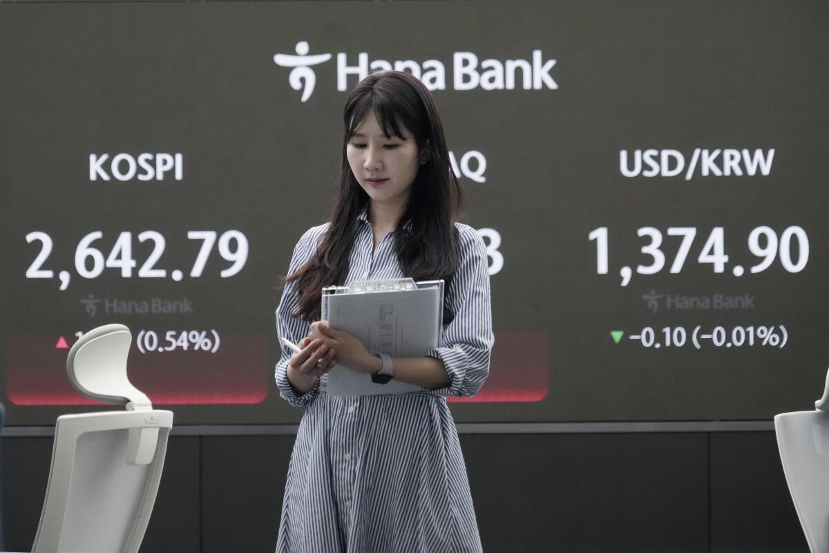 Una corredora de divisas pasa junto a una pantalla que muestra el índice KOSPI, a la izquierda, en la sede del KEB Hana Bank el viernes 26 de abril de 2024, en Seúl, Corea del Sur. (AP Foto/Ahn Young-joon)