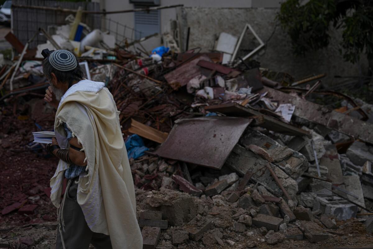 Man in prayer shawl passing pile of rubble from rocket strike