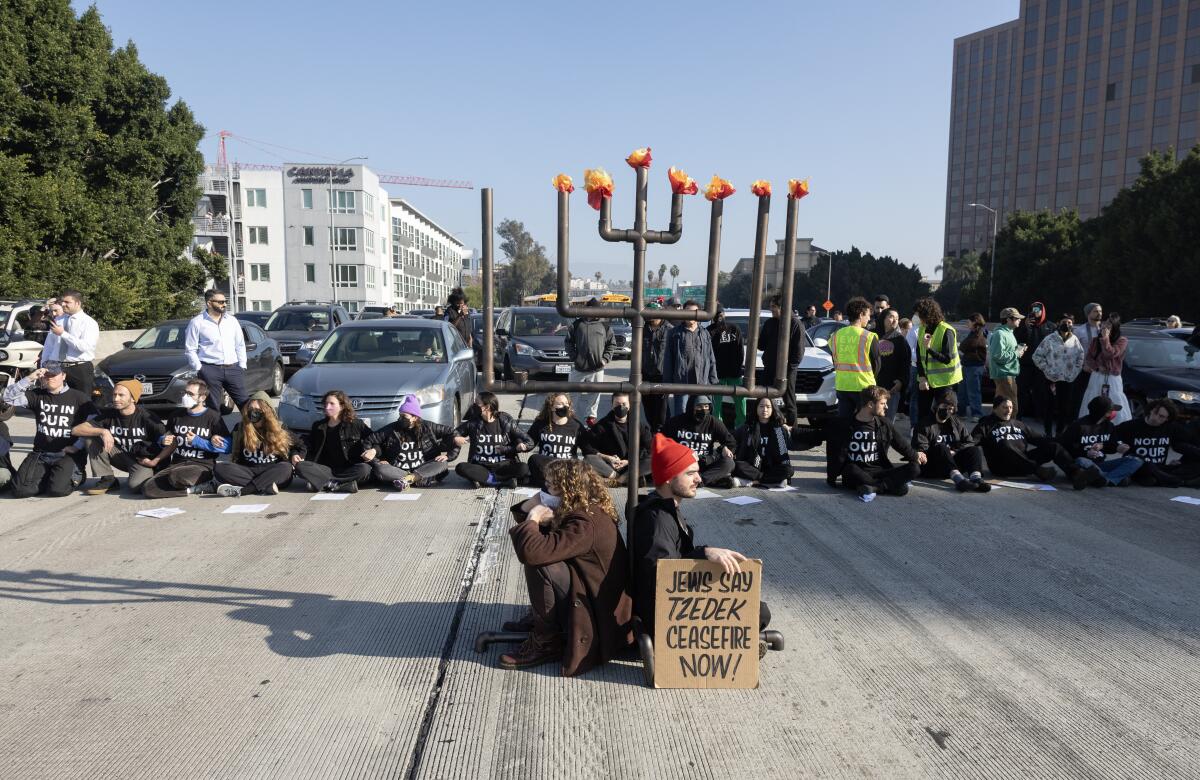 A line of protesters sitting on a freeway block traffic, with a seven-foot menorah in the middle