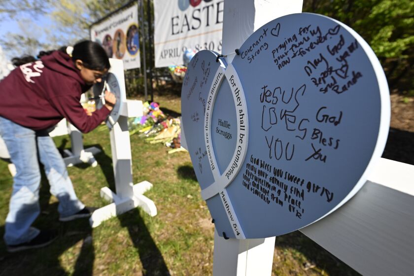 A youngster writes a message on crosses at an entry to Covenant School, Tuesday, March 28, 2023, in Nashville, Tenn., which has become a memorial to the victims of Monday's school shooting. (AP Photo/John Amis)