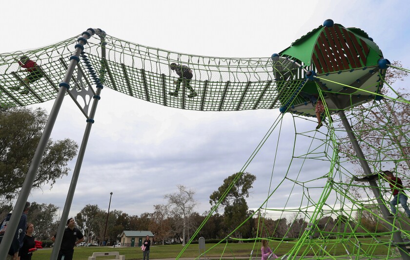 Kids test out the rope-tunnel bridge at the new children's Central Park Playground in Huntington Beach.