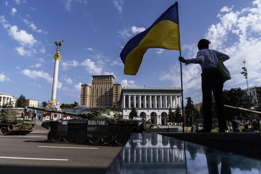 A woman holds the flag of Ukraine while looking over a row of destroyed Russian military vehicles on display at Maidan Square in Kyiv, Ukraine, Tuesday, Aug. 23, 2022. Kyiv authorities have banned mass gatherings in the capital through Thursday for fear of Russian missile attacks. Independence Day, like the six-month mark in the war, falls on Wednesday. (AP Photo/David Goldman)