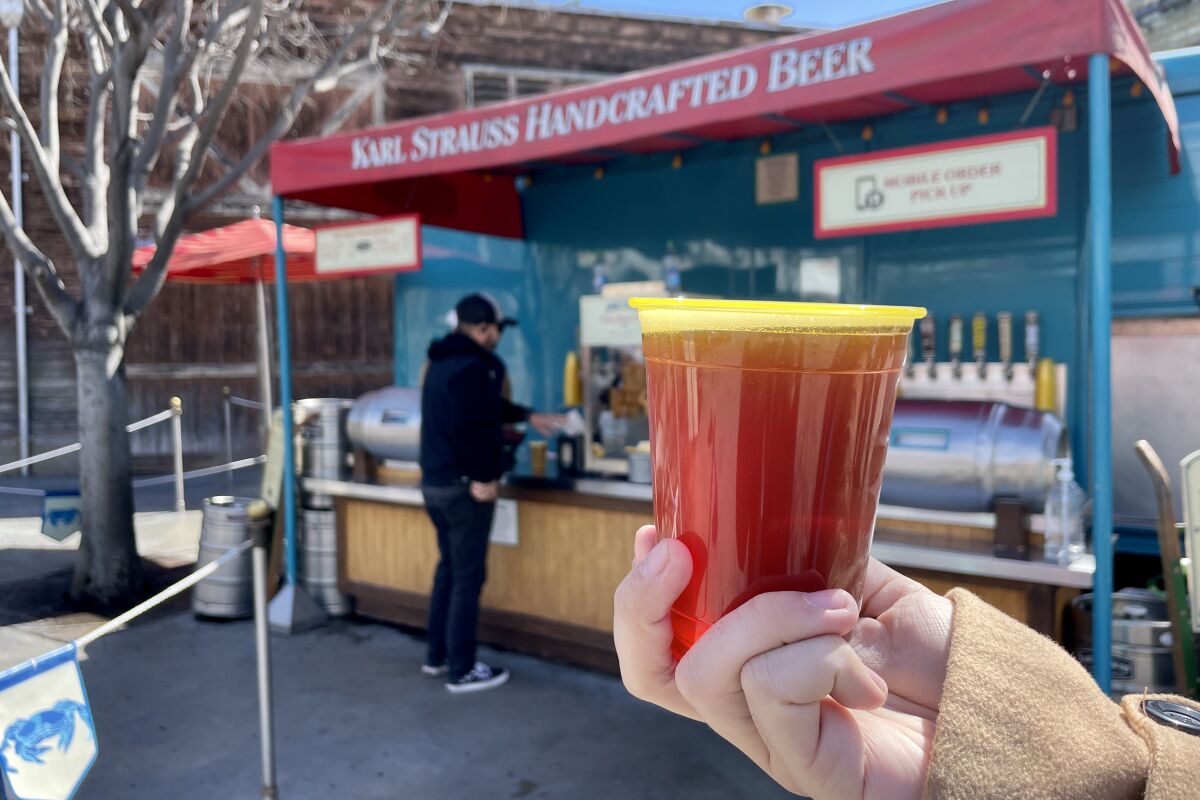 A hand holds up a plastic cup of Karl Strauss Brewing Co. Red Trolley Ale in front of the beer truck.