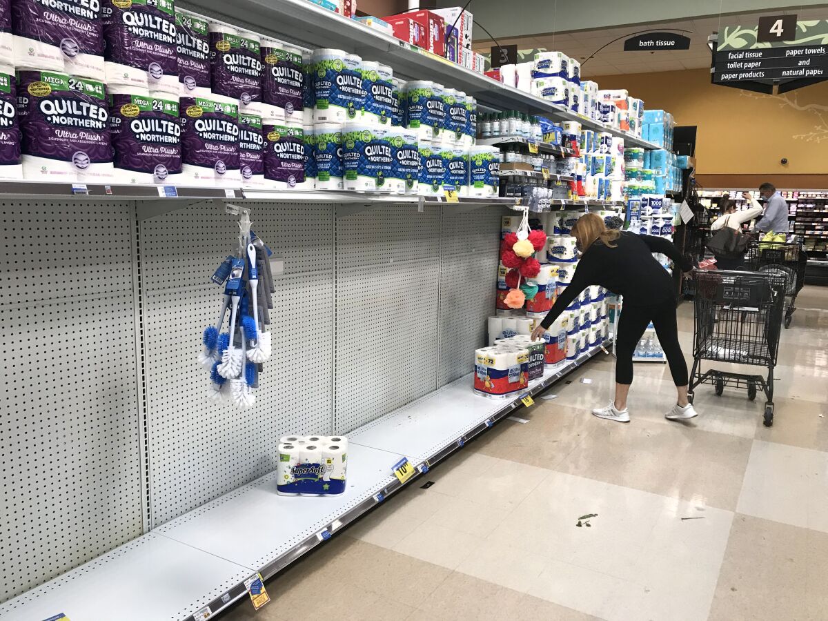 A shopper reaches for a roll of toilet paper on a partially empty shelf at Ralph's market in Calabasas. 