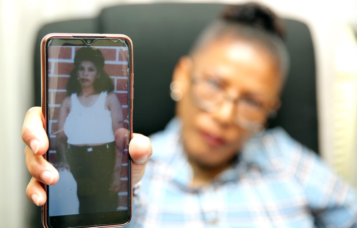 A woman holds up a cellphone displaying a photo of a younger woman