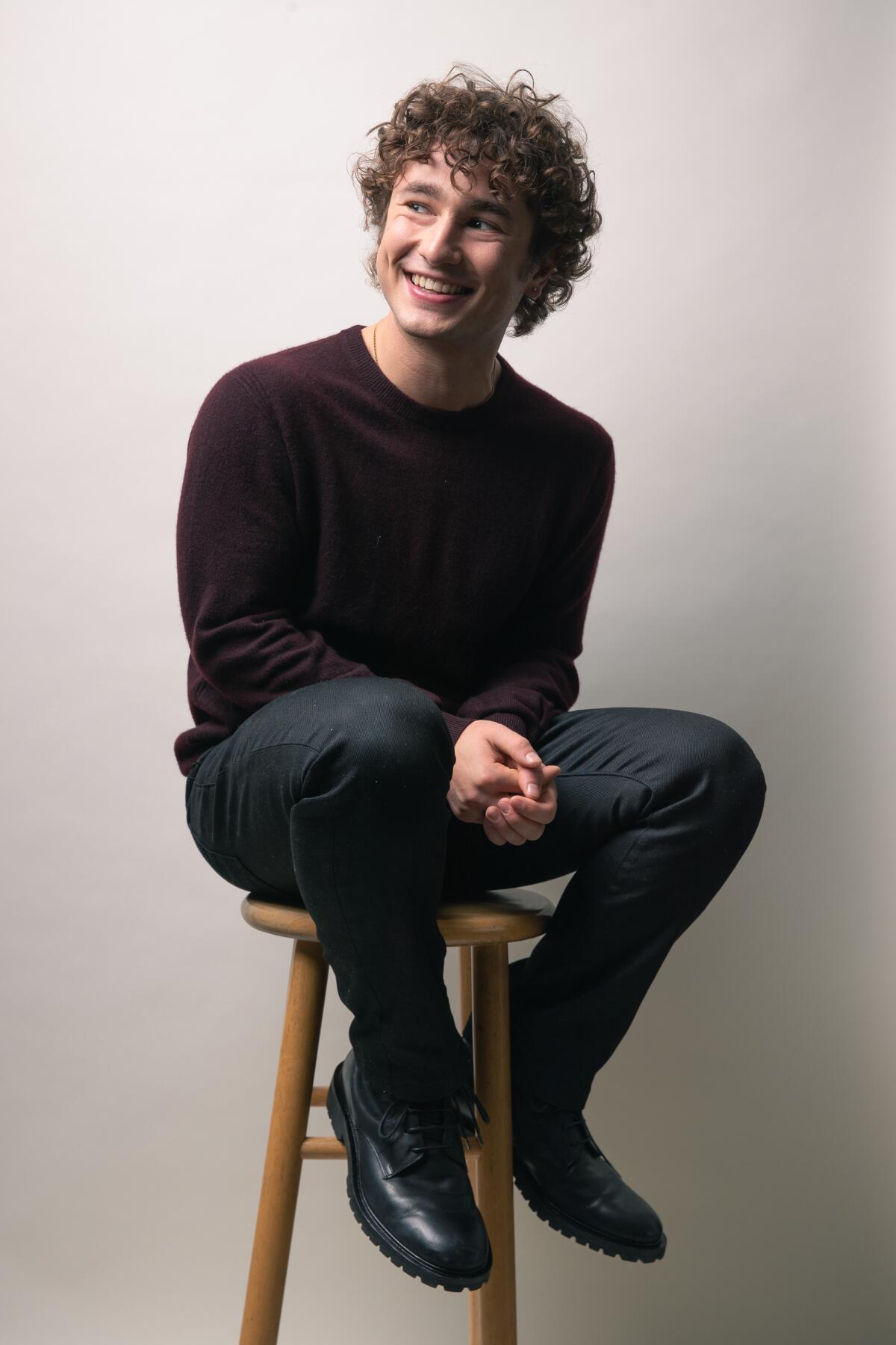 Gabriel LaBelle smiles as he sits on a stool.