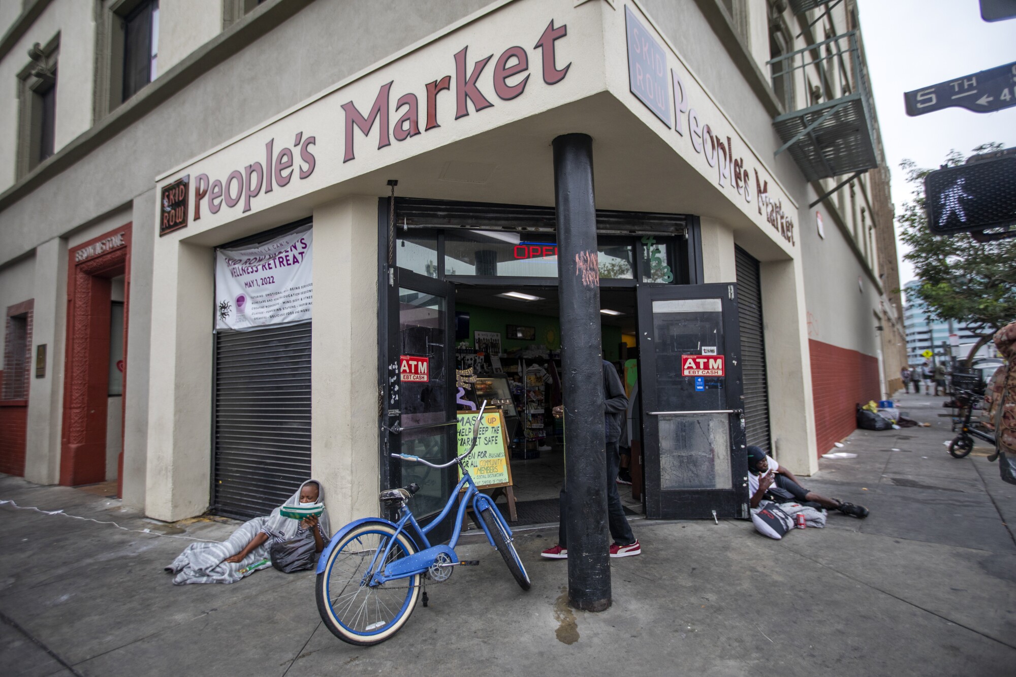 A woman and a man lie on the sidewalk outside the entrance of Skid Row People's Market. 