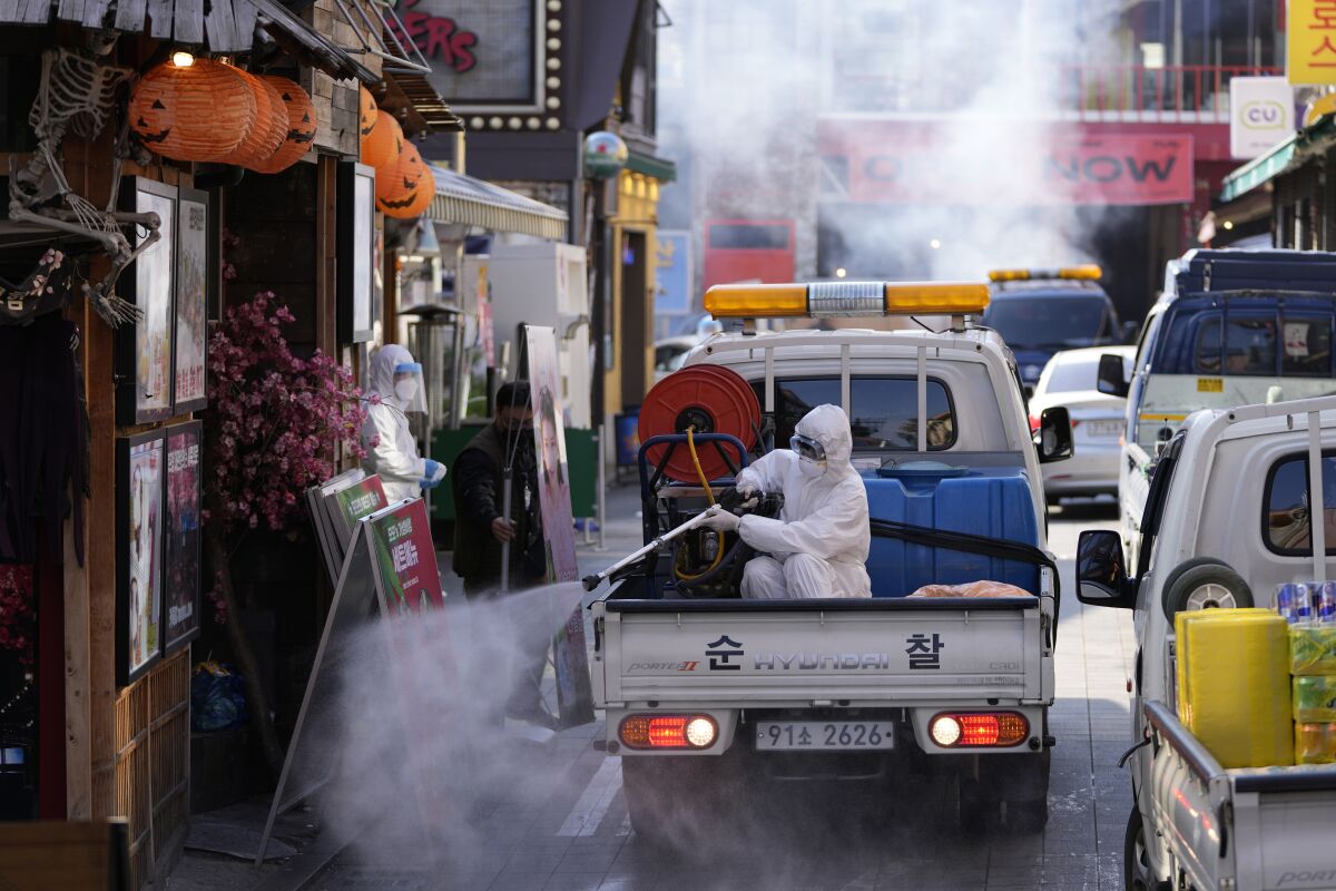 FILE - A local district health official in protective gear disinfects shop fronts as a precaution against the coronavirus in Seoul, South Korea, Friday, Oct. 29, 2021. South Korea has allowed larger social gatherings and lifted business-hour restrictions on restaurants starting Monday, Nov. 1, 2021, in what officials describe as the first step of an attempt to restore some pre-pandemic normalcy. (AP Photo/Lee Jin-man, File)