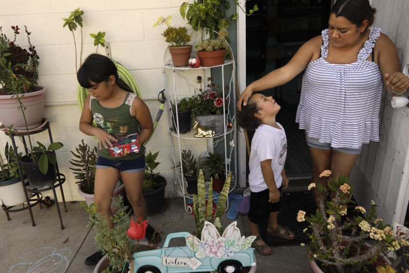 PACOIMA, CA - JUNE 16, 2021 - - Lizette Romo Gonzalez, 31, wipes the sweat off her son's brow while trying to cool off in front of their unit at the San Fernando Gardens Public Housing where temperatures rose to 94 degrees in Pacoima on June 16, 2021. Gonzalez lives in the unit with her husband and five children. She said it was so hot recently that she put all her children in a bathtub of ice cubes and water. That didn't go so well and all the children came down with colds. It was the last time she tried that method. As with other climate-related disasters, the consequences are hugely unequal falling disproportionately on poor communities, like The Gardens, where trees are scarce and residents don't have air conditioning or can't afford to run it. Apartments in public housing do not come with air conditioning and residents have to buy their own, use fans or buy swamp coolers. The families that do have air conditioning use them sparingly to keep their energy bills affordable. (Genaro Molina / Los Angeles Times)