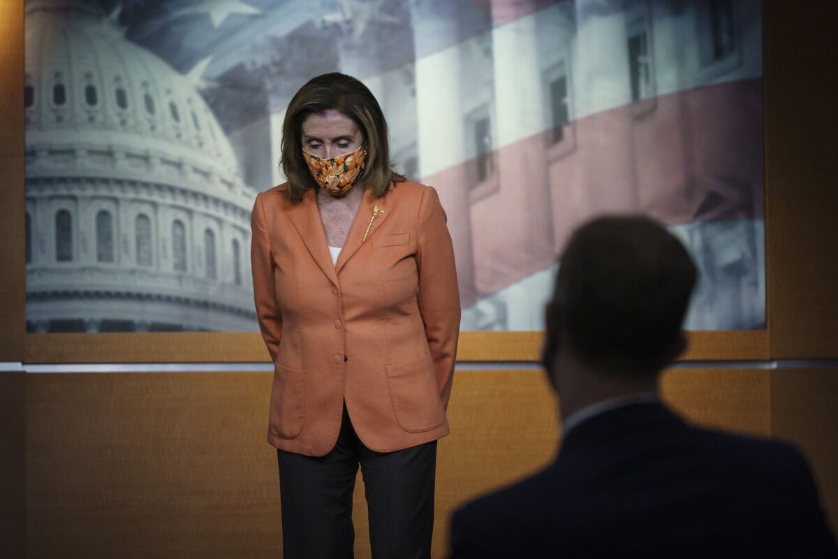 Nancy Pelosi, wearing a mask, stands before a reporter at the Capitol.