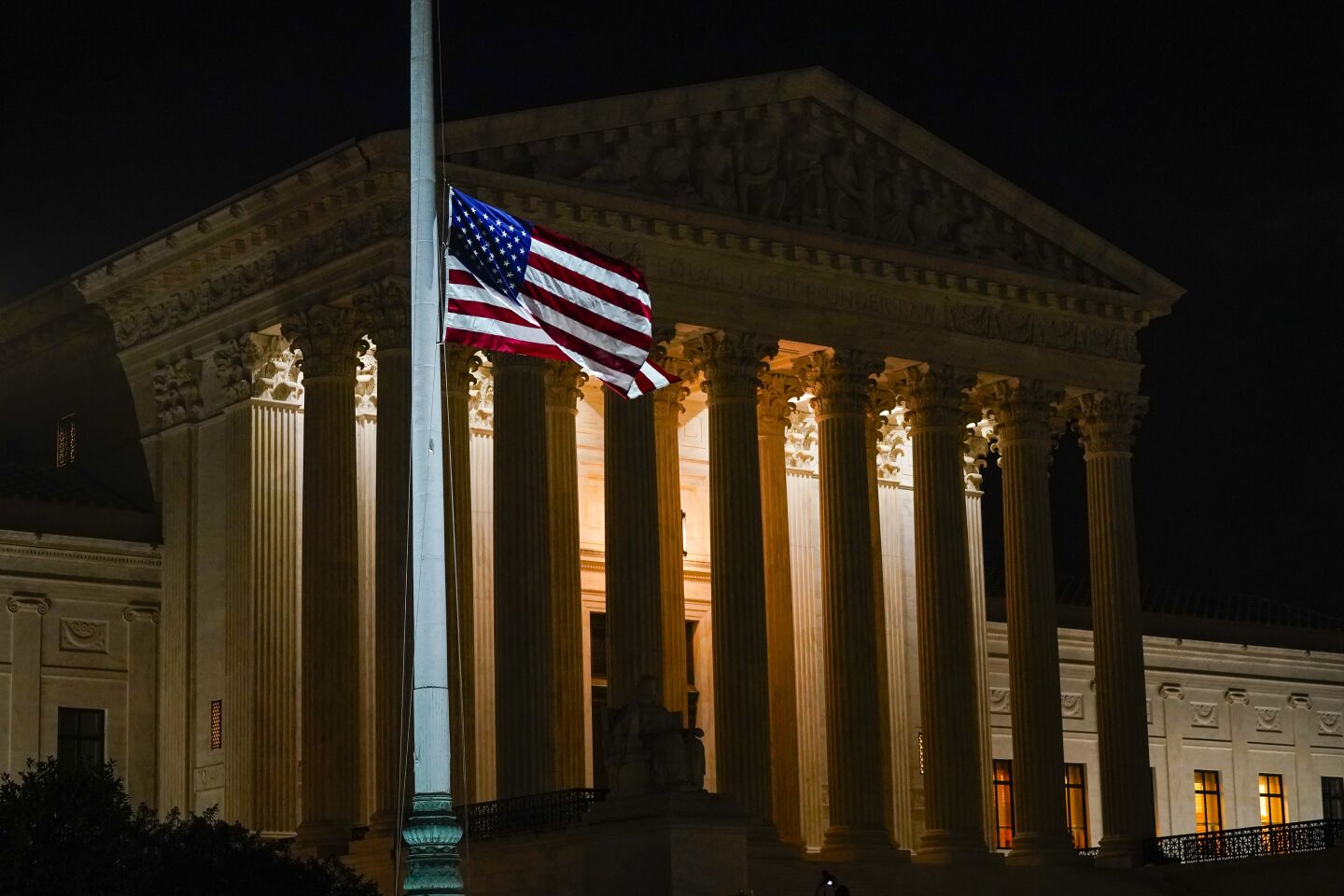 The U.S. flag blows in the wind at half-staff at night in front of the Supreme Court building