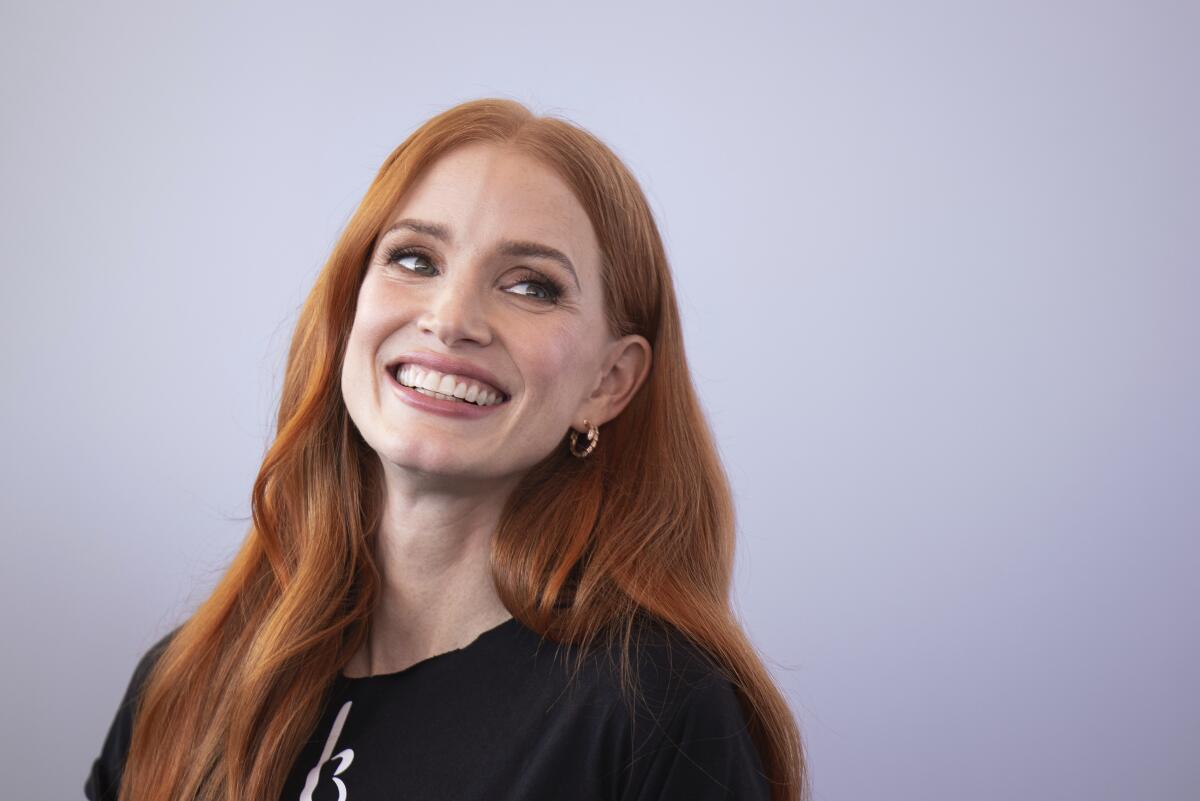 A woman with red hair smiling in a black T-shirt against a light backdrop