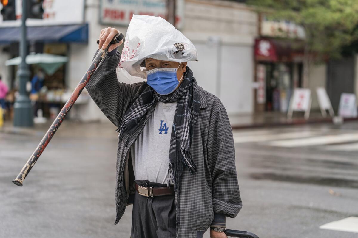 A pedestrian protects his hat from the rain with a plastic bag in the Chinatown district of Los Angeles, Monday, Nov. 7, 2022. A new Pacific storm is bringing snow, rain and wind to California. It’s the second significant storm this month for the state, which remains deep in drought. (AP Photo/Damian Dovarganes)