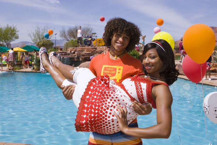 A man holds a woman in a poolside “High School Musical” moment.