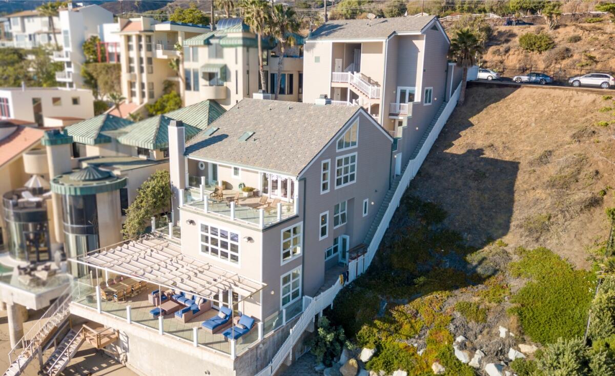 The exterior of the contemporary Cape Cod with multiple decks overlooking the ocean and an empty hillside next to it.