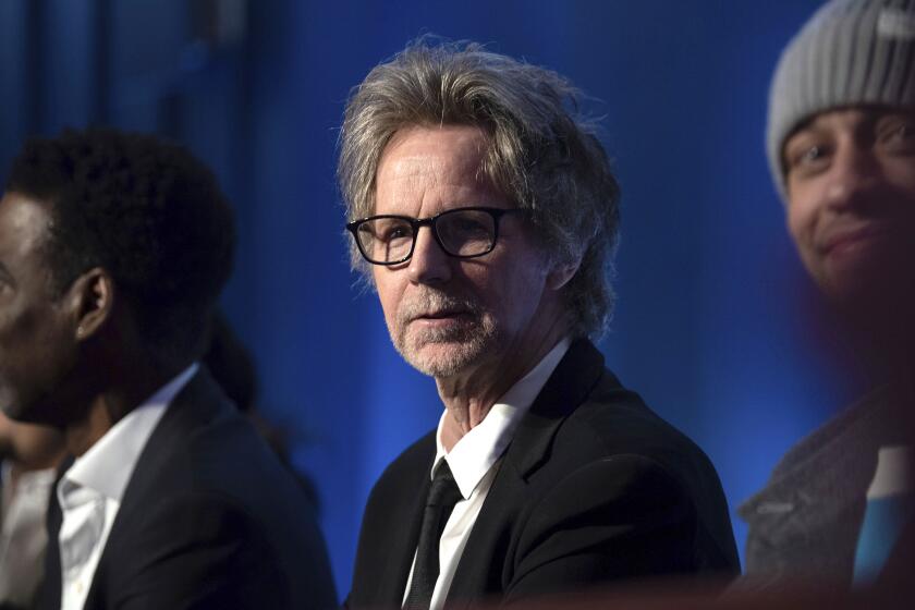 Dana Carvey looks out over the crowd while wearing a black suit and black-framed glasses