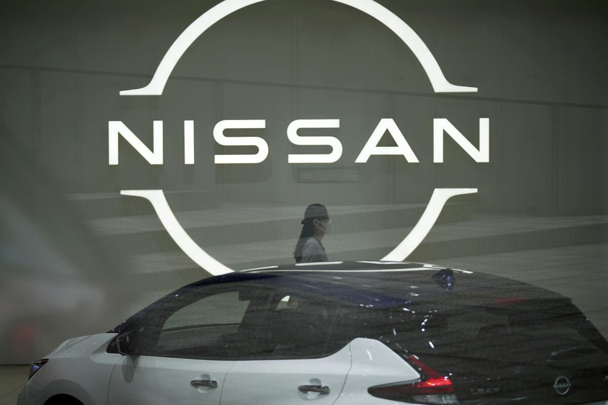 FILE - A staff walking near a Nissan logo at Nissan headquarters is seen though a window on May 12, 2022, in Yokohama near Tokyo. Nissan’s profit fell 68% in the last quarter as a shortage of computer chips hindered the Japanese automaker’s ability to deliver vehicles to its customers.(AP Photo/Eugene Hoshiko, File)