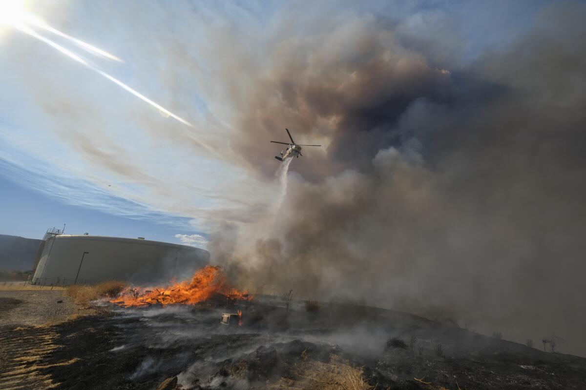 A helicopter drops water on a wildfire.