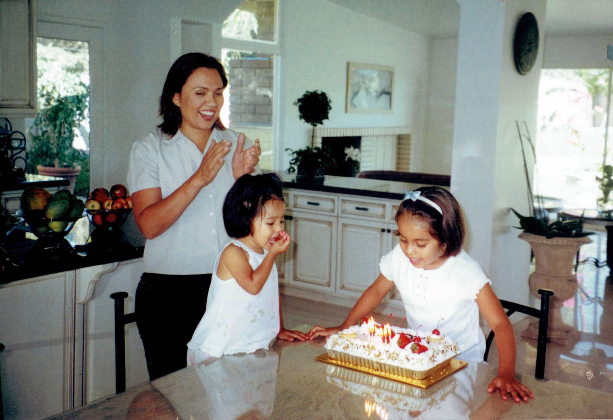 Gloria Verduzco claps as her eldest daughter, Ilianna Salas, blows out birthday candles and her youngest daughter watches.