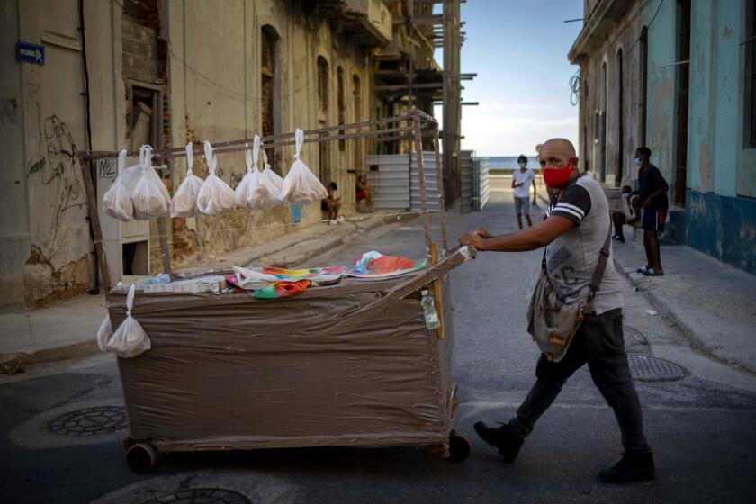 A street vendor wearing a mask as a precaution against the spread of the new coronavirus pushes his cart down a street in Havana, Cuba, Monday, Aug. 31, 2020. Cuban authorities will introduce new measures starting tomorrow Tuesday aimed at containing the spread of the coronavirus in Havana among others a curfew from 7 pm until 5 am and no one without special permission will be able to enter or leave the province. The new measures will last at least 15 days. (AP Photo/Ramon Espinosa)
