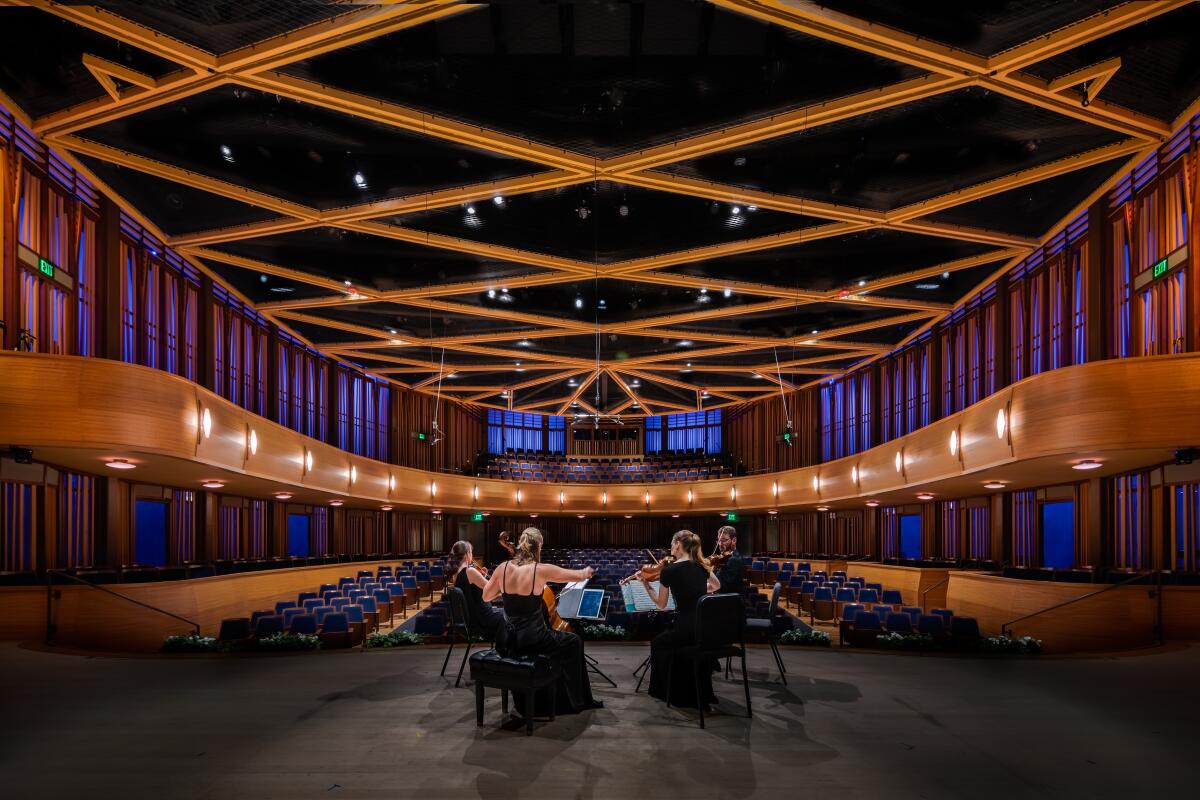 A quartet of string musicians plays on stage before an empty theater lined in wood