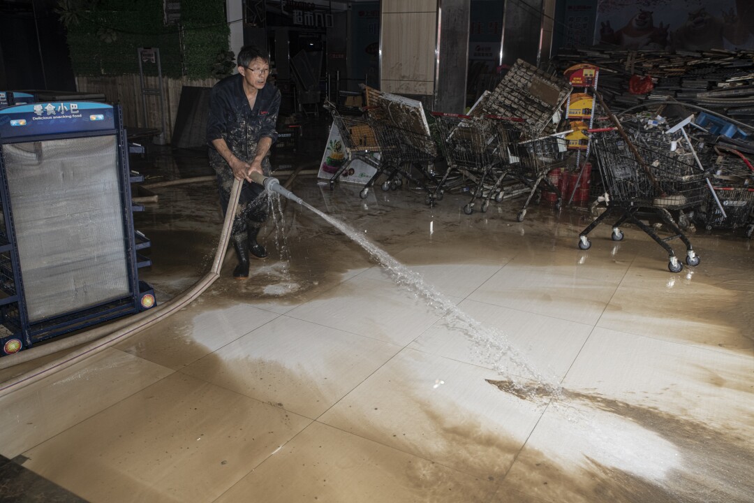 An employee washes away mud from the floor of a flooded supermarket in Shexian, Anhui province.