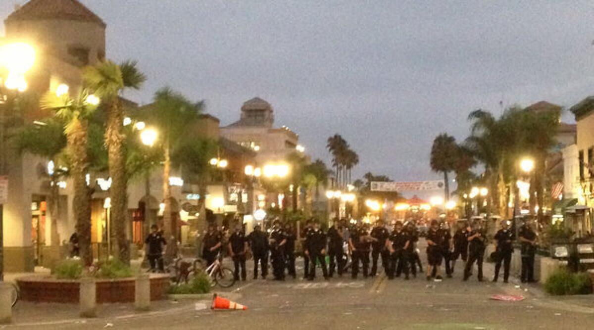 Police in riot gear converge on downtown Huntington Beach Sunday evening to break up an unruly crowd that had gathered following the U.S. Open of Surfing.