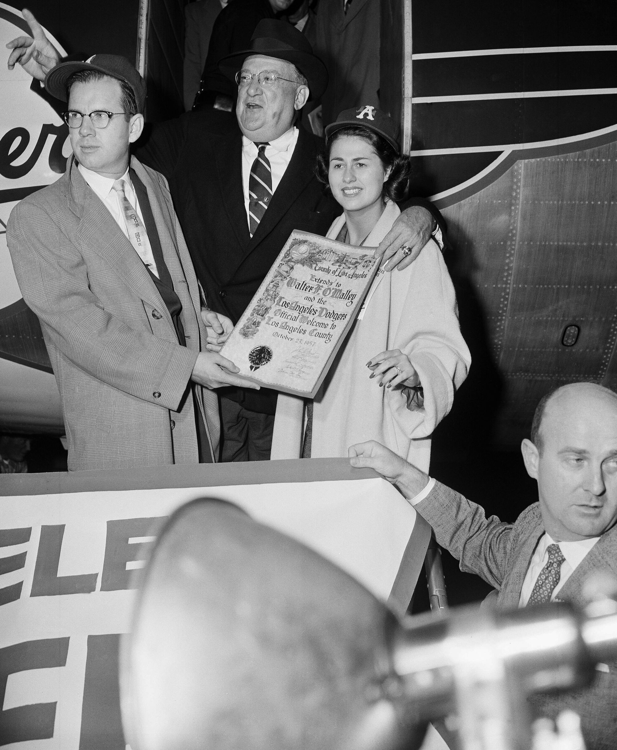 Walter O'Malley stands between Kenneth Hahn and Rosalind Wyman as they hold up a document.