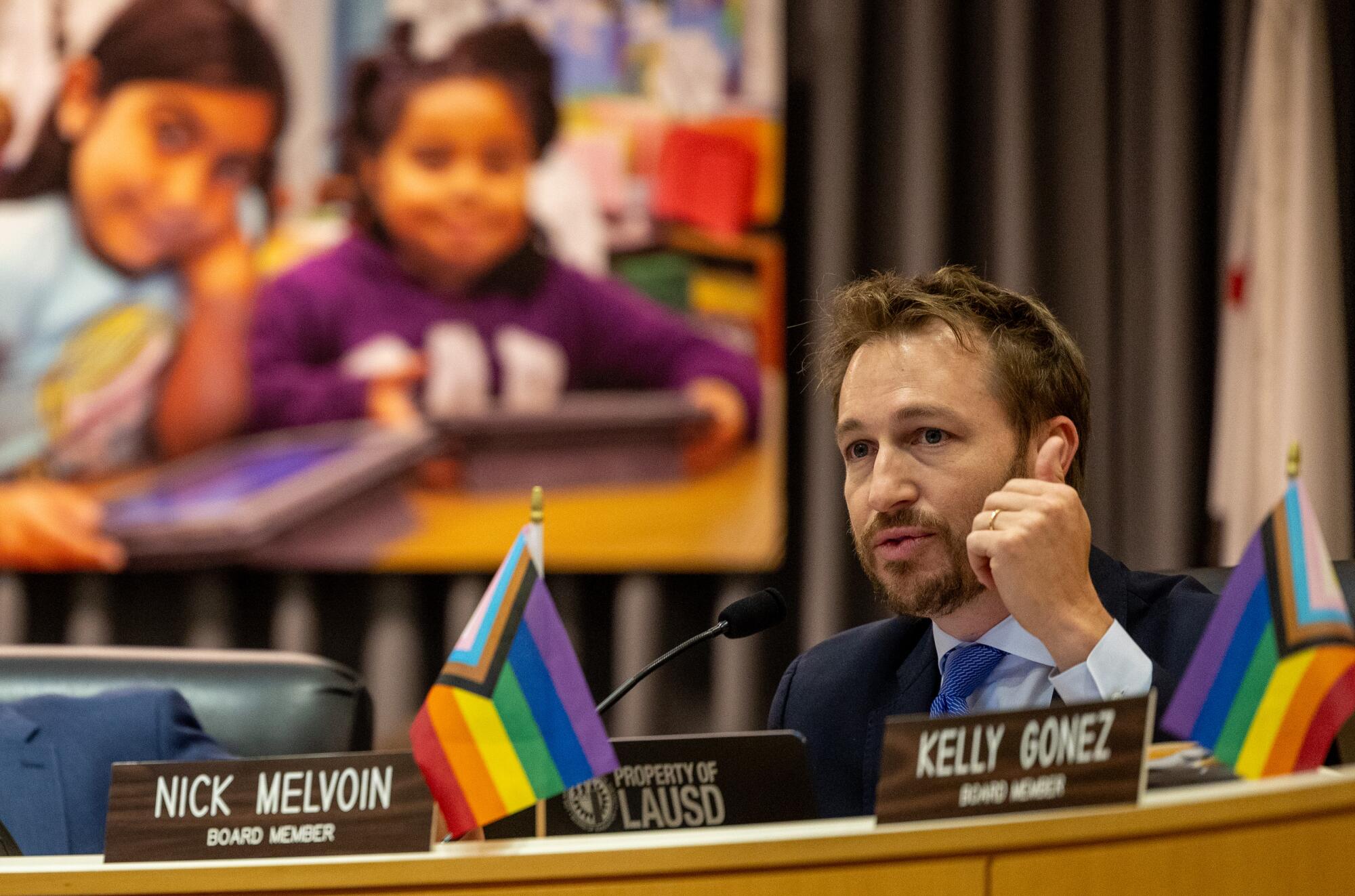 A male school board member speaks into a microphone at a meeting. 