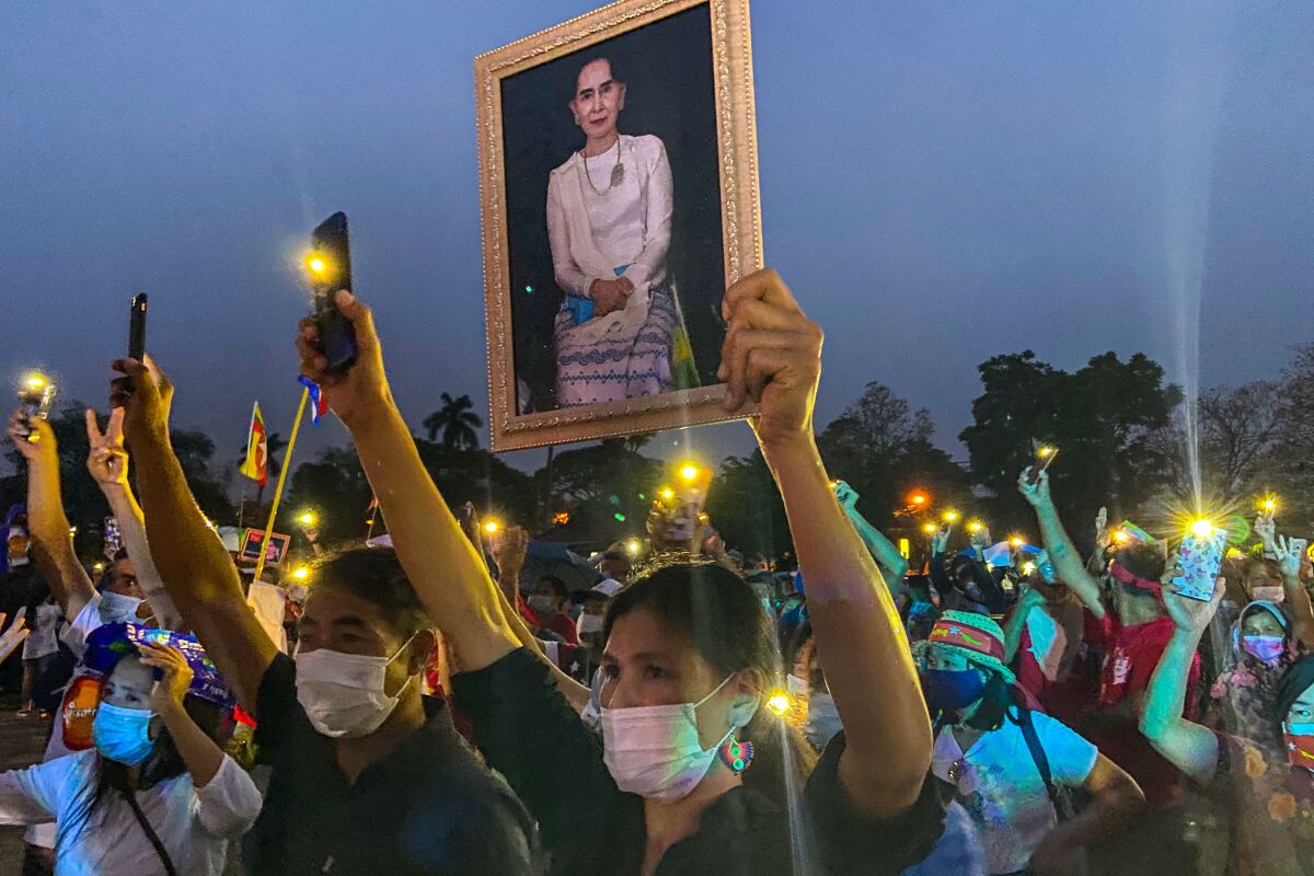 A person holds up a portrait of  Aung San Suu Kyi among a crowd of people holding up cellphone flashlights. 