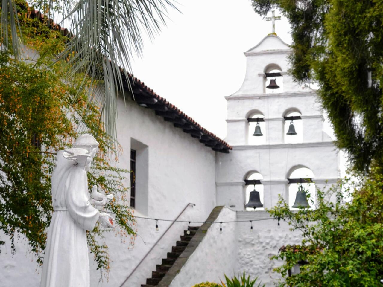 Las campanas de la misión San Diego de Alcalá. La campana en la parte inferior izquierda es Mater Dolorosa, Nuestra Señora de los Dolores, de 1,200 libras, la más pesada de las cinco. Fue refundido en la década de 1890. Suena a diario. La estatua a la izquierda es San Francisco.