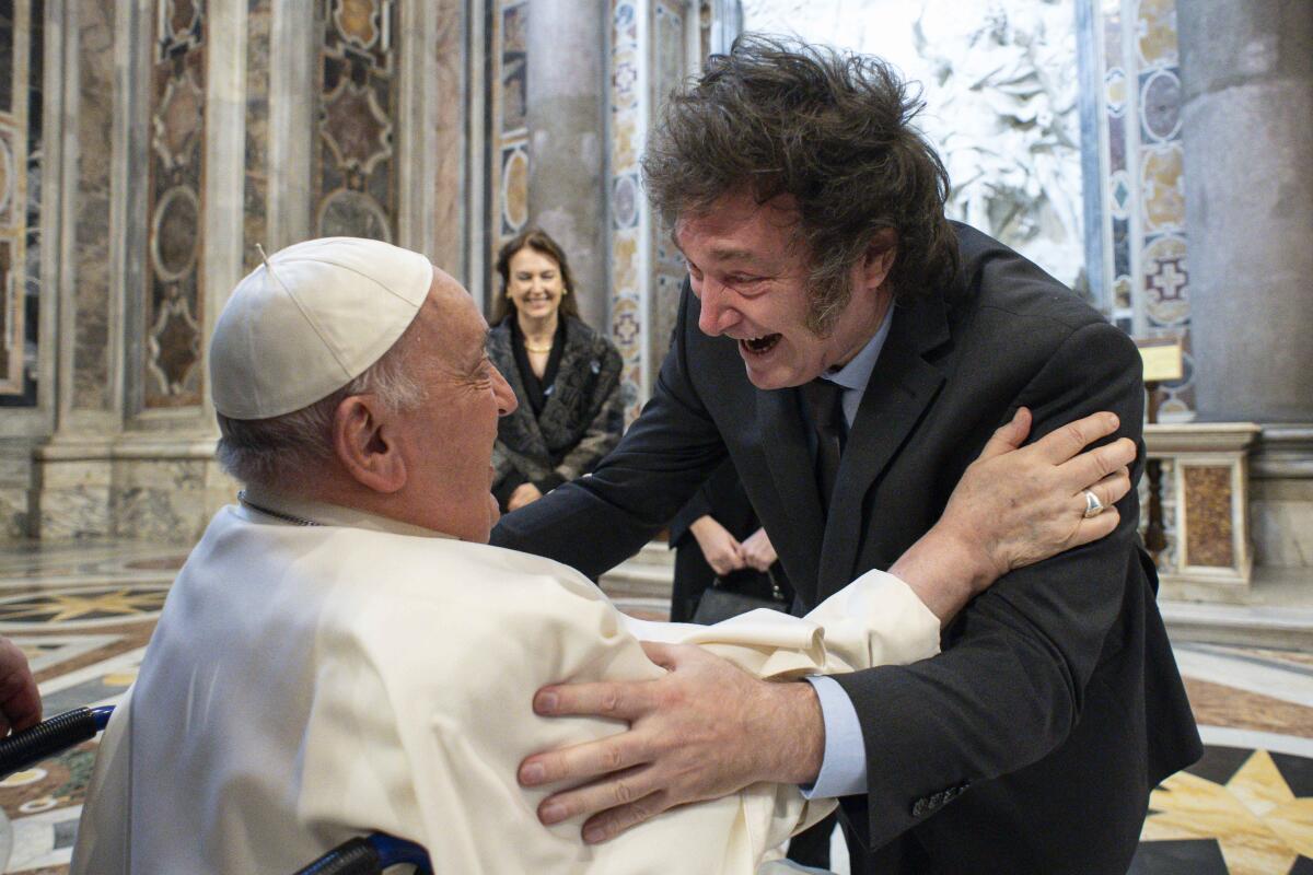Argentine President Javier Milei and Pope Francis reach out their arms to each other in an ornate room.
