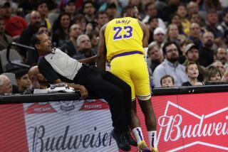 Referee Eric Lewis, left, and Lakers' LeBron James (23) crash into the scorer's table during a game.