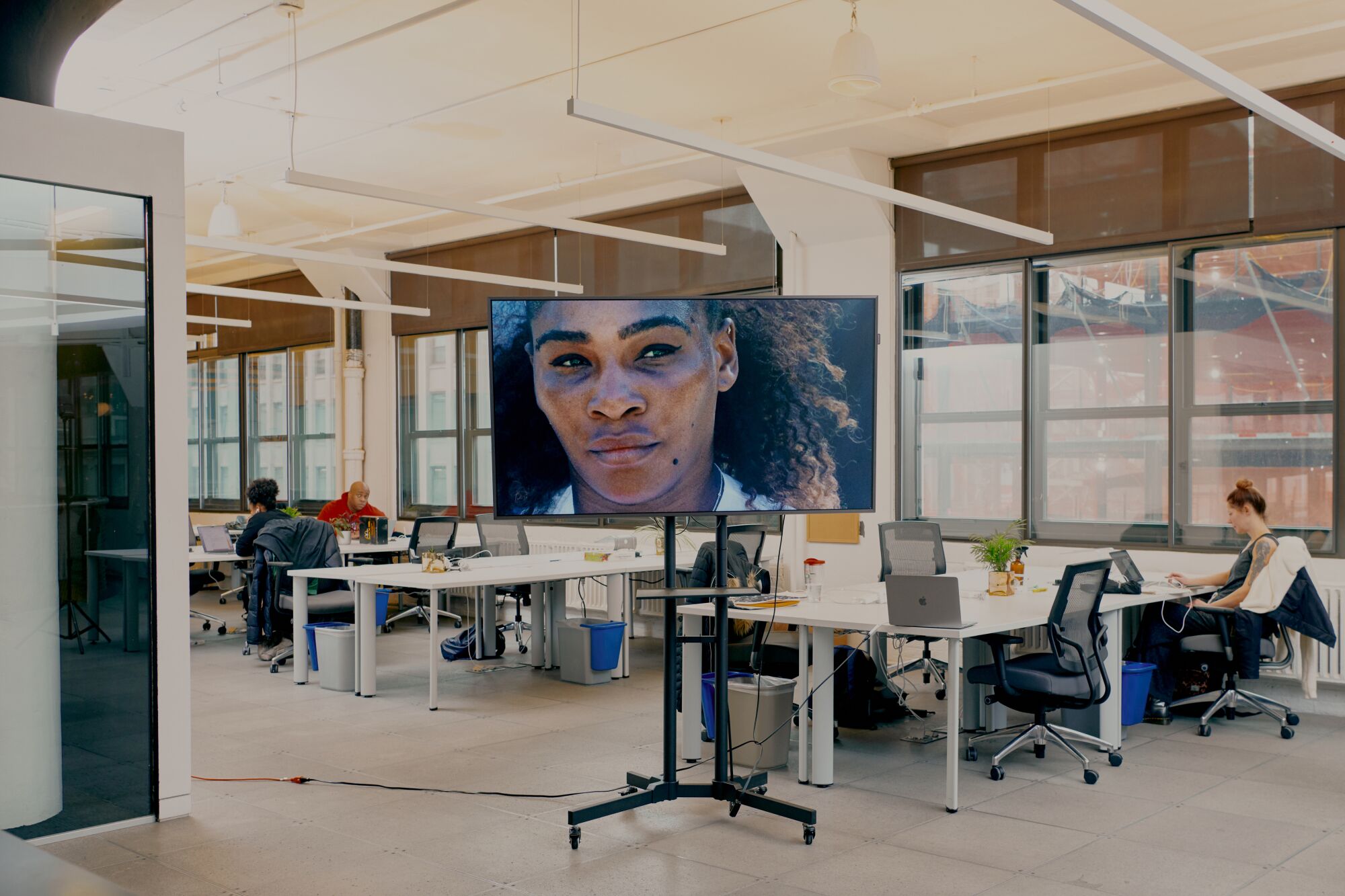 In an office with an open floor plan, a television plays an ad starring Serena Williams.