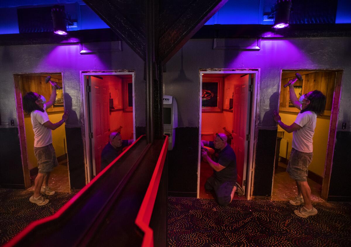 Two men work on door frames in a dark bar.