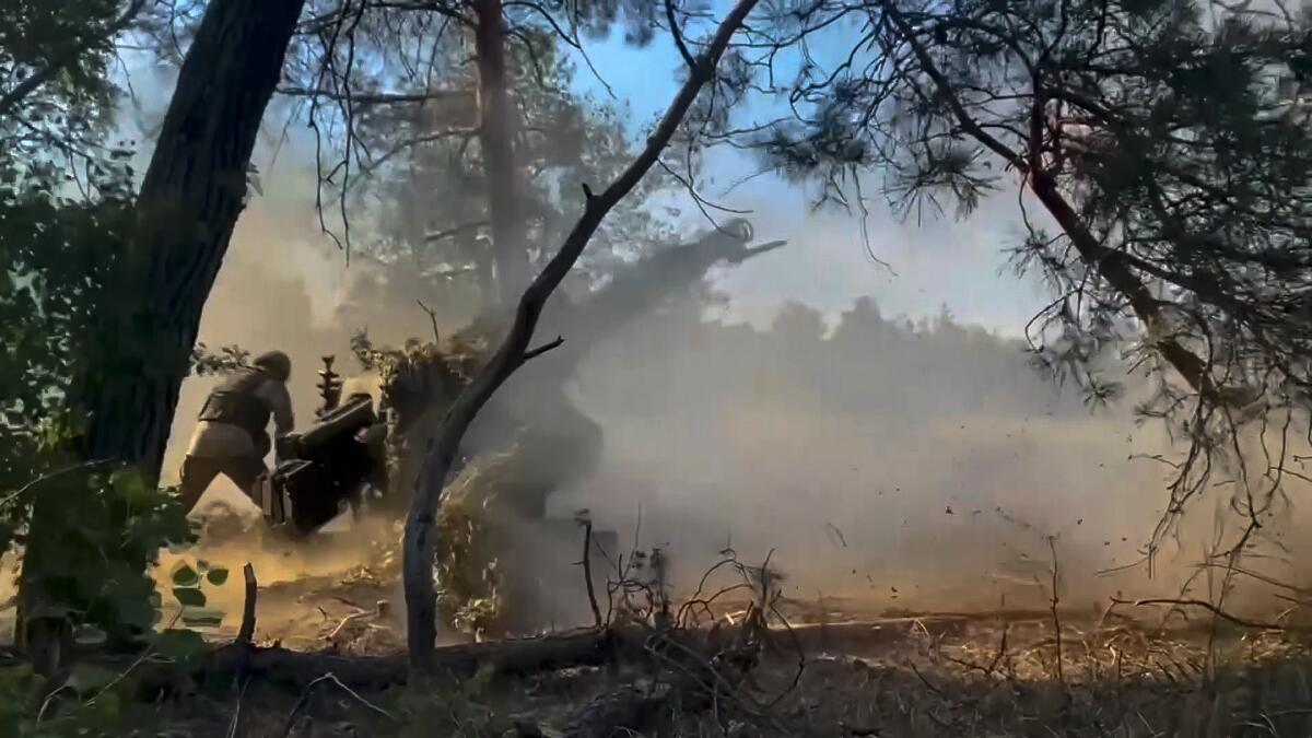 Russian soldiers fire a howitzer amid smoke. 