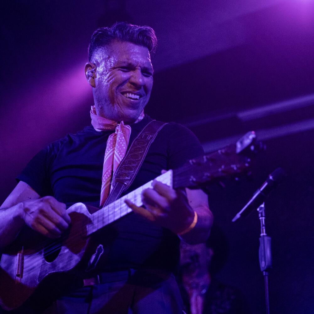 A smiling man is bathed in blue light during a performance.