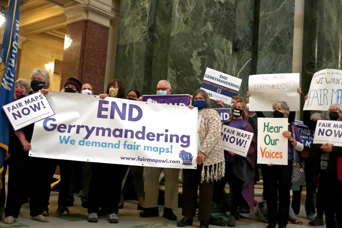 People hold signs reading, "End gerrymandering" and "Fair maps now."