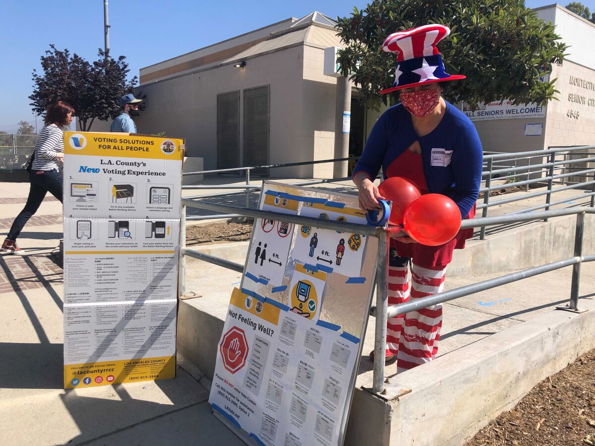 Camille Teran-Grange, a volunteer at polling place at the Montecito Heights Senior Citizen Center in Los Angeles, adds balloons to voter information placards on Tuesday, Sept. 14, 2021. (AP Photo/Stefanie Dazio)