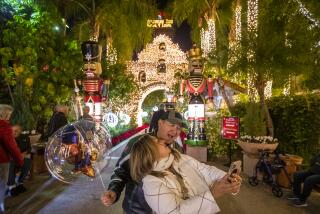 Riverside, CA - December 08: Linda and Joe Rodriguez, of Fontana, take photos among the sights and sounds of the 29th annual Festival of Lights display which features Christmas-themed displays, fake falling snow and roaming carolers performing for diners at the restaurants at the historic Mission Inn Hotel & Spa in Riverside on Wednesday, Dec. 8, 2021. The Inn's six-week holiday merriment continues to Thursday, January 6, 2022. The popular annual tradition was first created in 1992 as a gift back to the community by the owners and keepers of the Inn, Kelly & Duane Roberts. (Allen J. Schaben / Los Angeles Times)