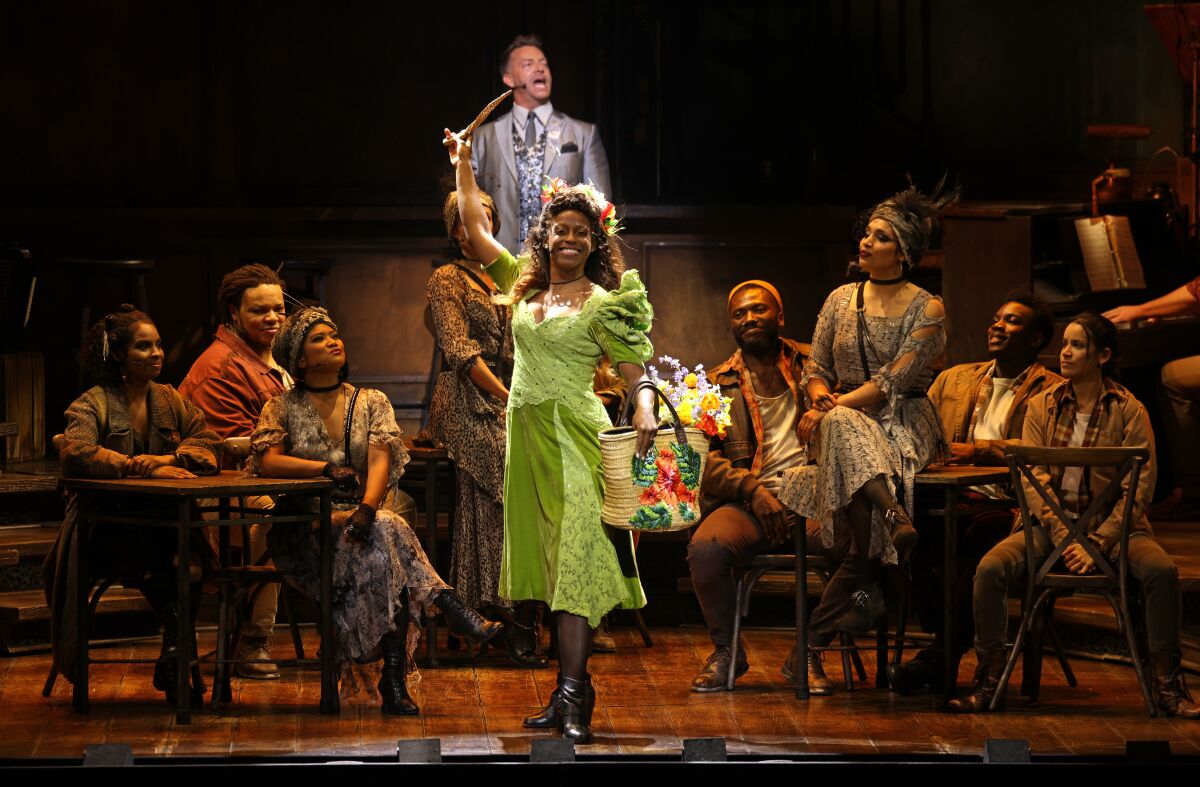 A woman in a green dress onstage with musicians and actors behind her.