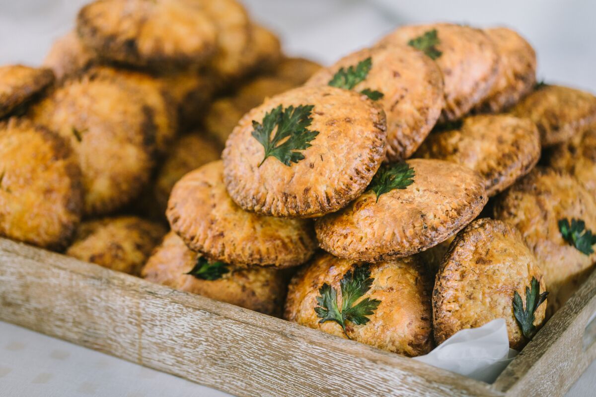 A photo of a tray piled with round, rustic small hand pies each topped by a leaf of parsley.