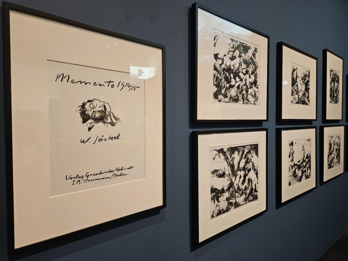 Seven lithographs on paper are hung on a gray museum wall; the first shows a severed head on its side.