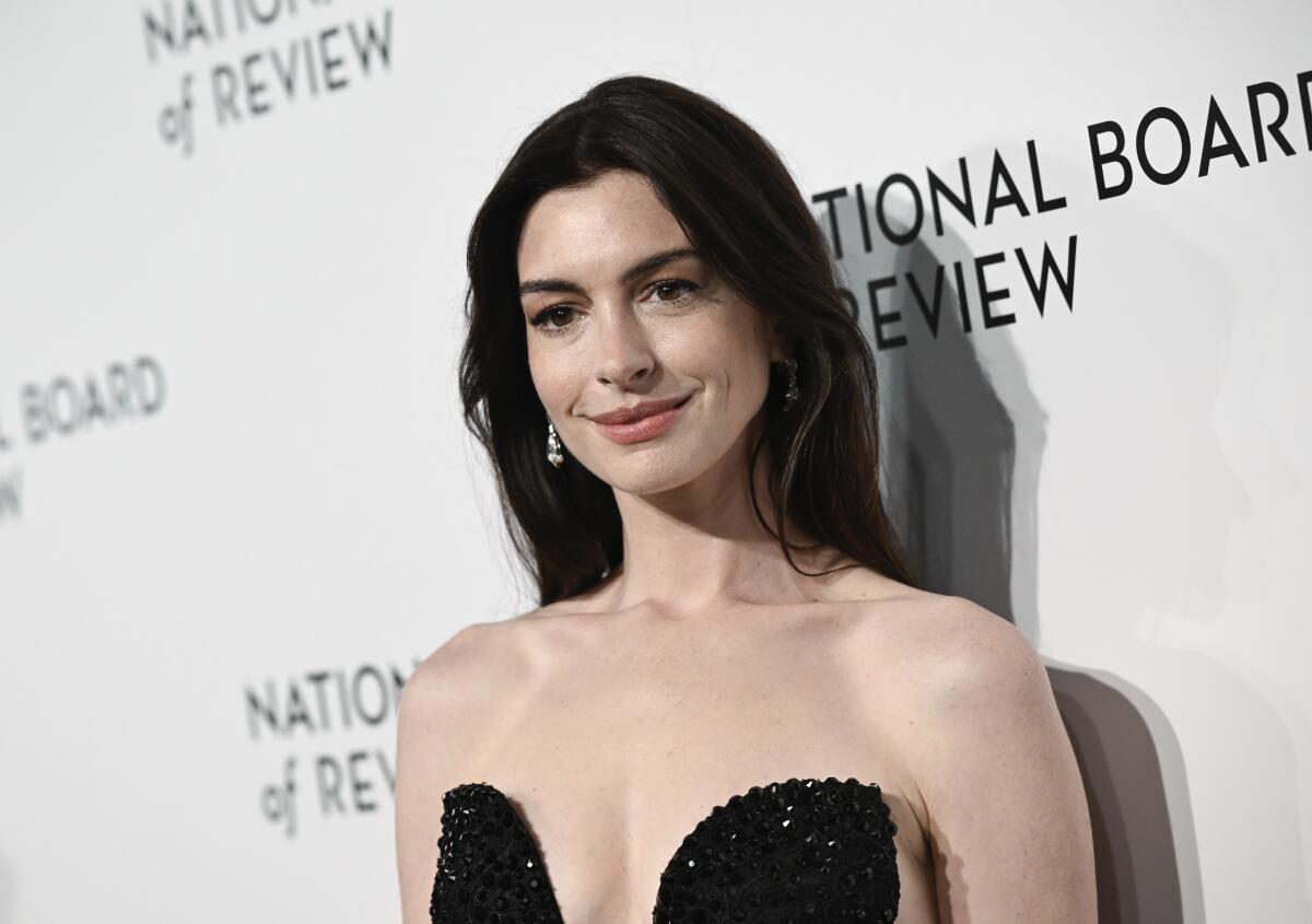 Anne Hathaway smiles peacefully while wearing a plunging, strapless black sequined gown