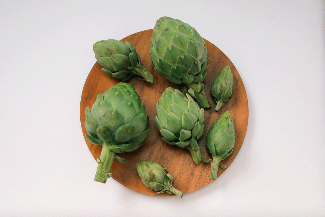 Animated artichokes of various sizes moving around on a round wooden plate