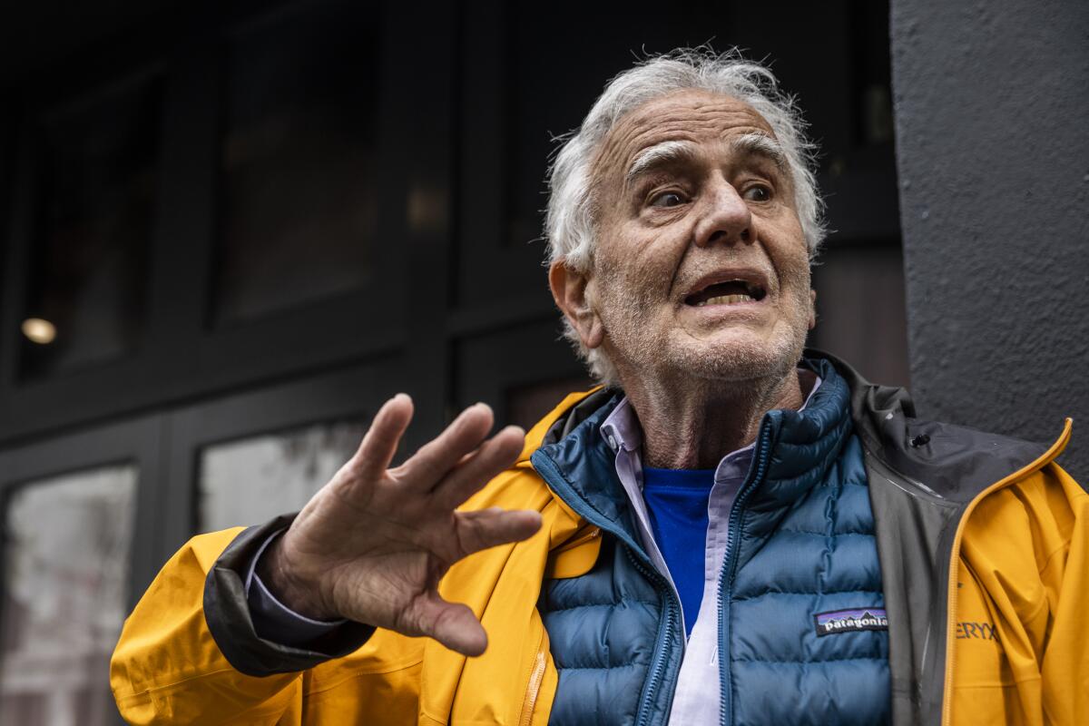 A man wearing a yellow jacket gestures while speaking