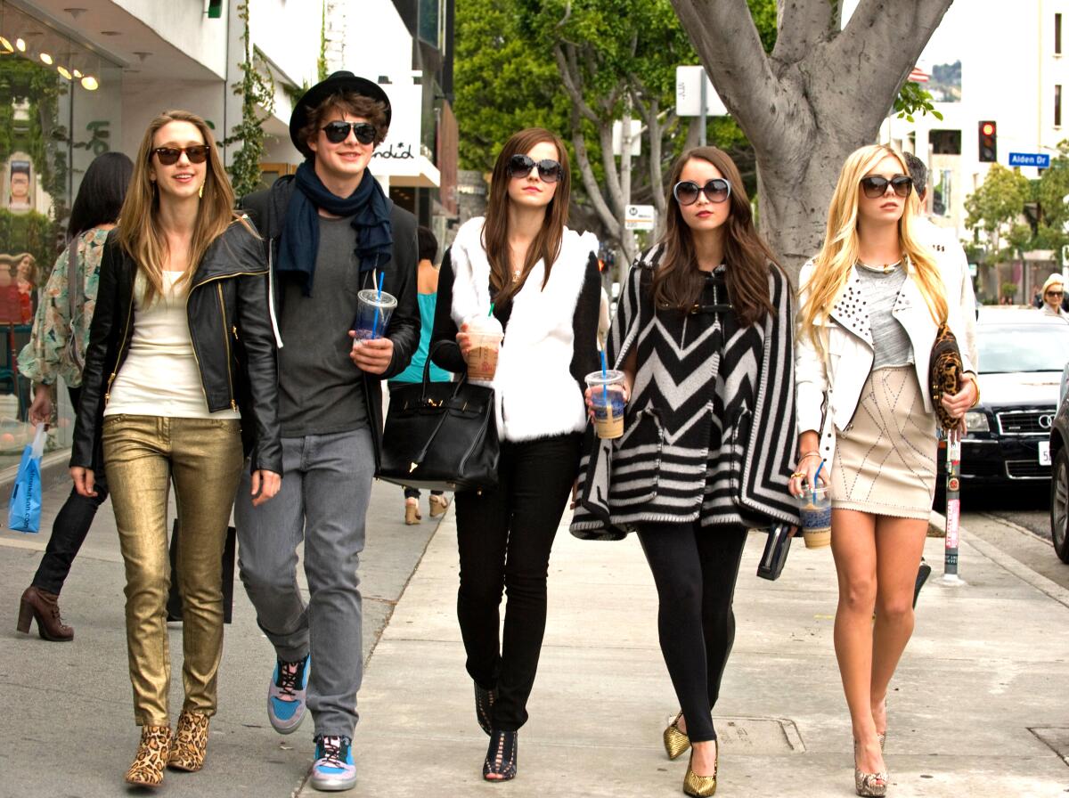 Five fashionably dressed young people walk on a sidewalk.