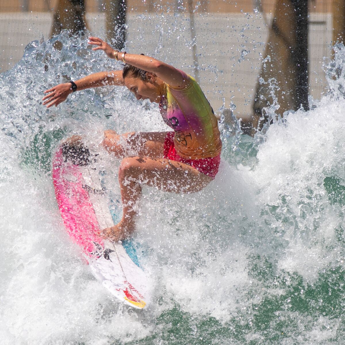A woman riding a wave on a pink, white and blue surf board