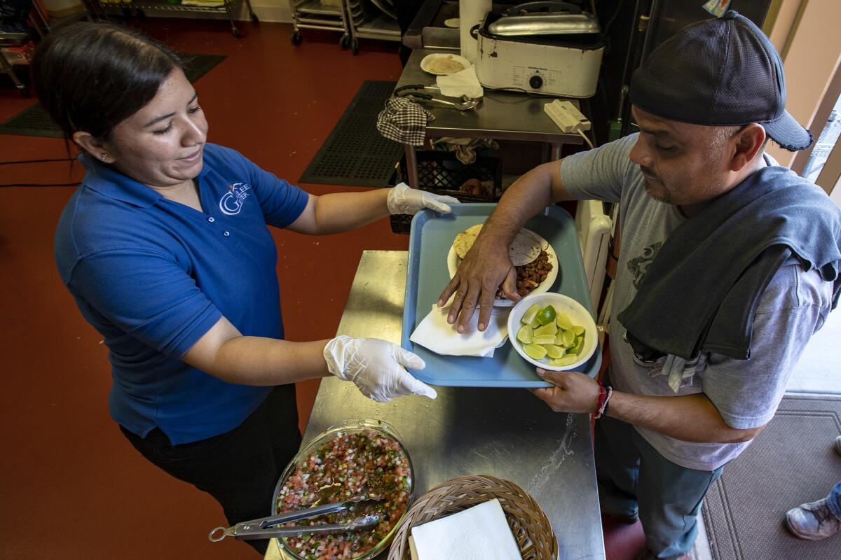 Jazmine Santiago, left, serves dinner to migrant farmworker Ricardo Martinez at Our Lady of Guadalupe shelter in Mecca.(Irfan Khan / Los Angeles Times)