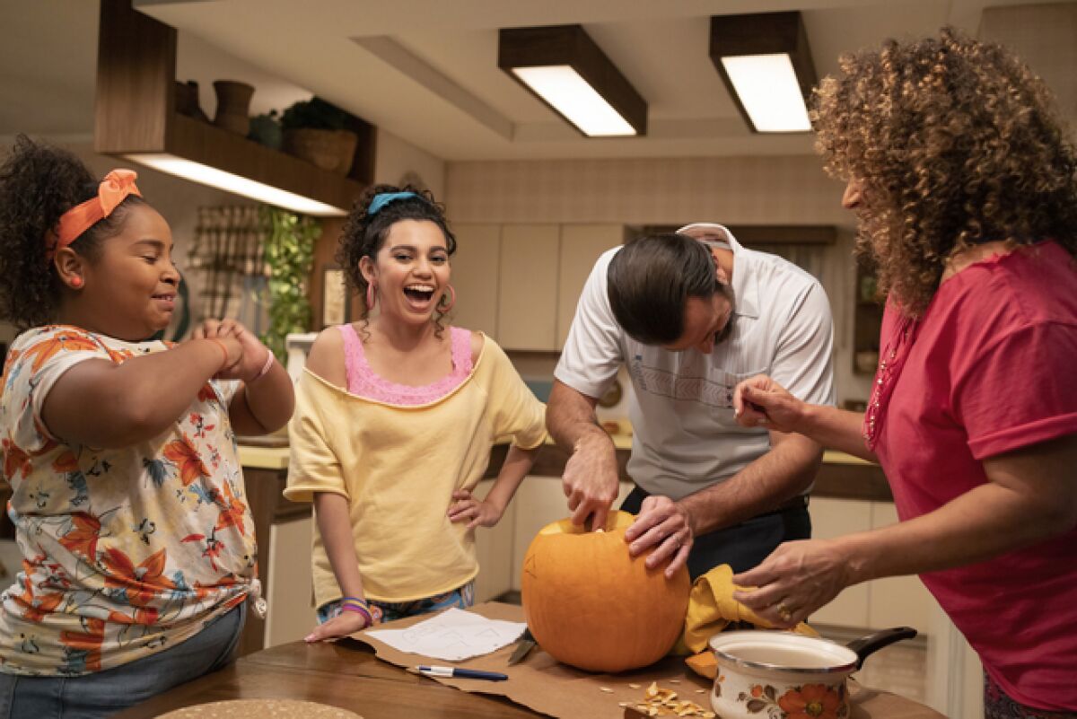 A family laughs as they carve a Jack-o'-lantern together.